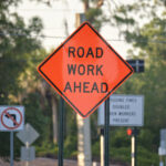 Warning roadworks sign and safety barrier on city street during maintenance repair work.